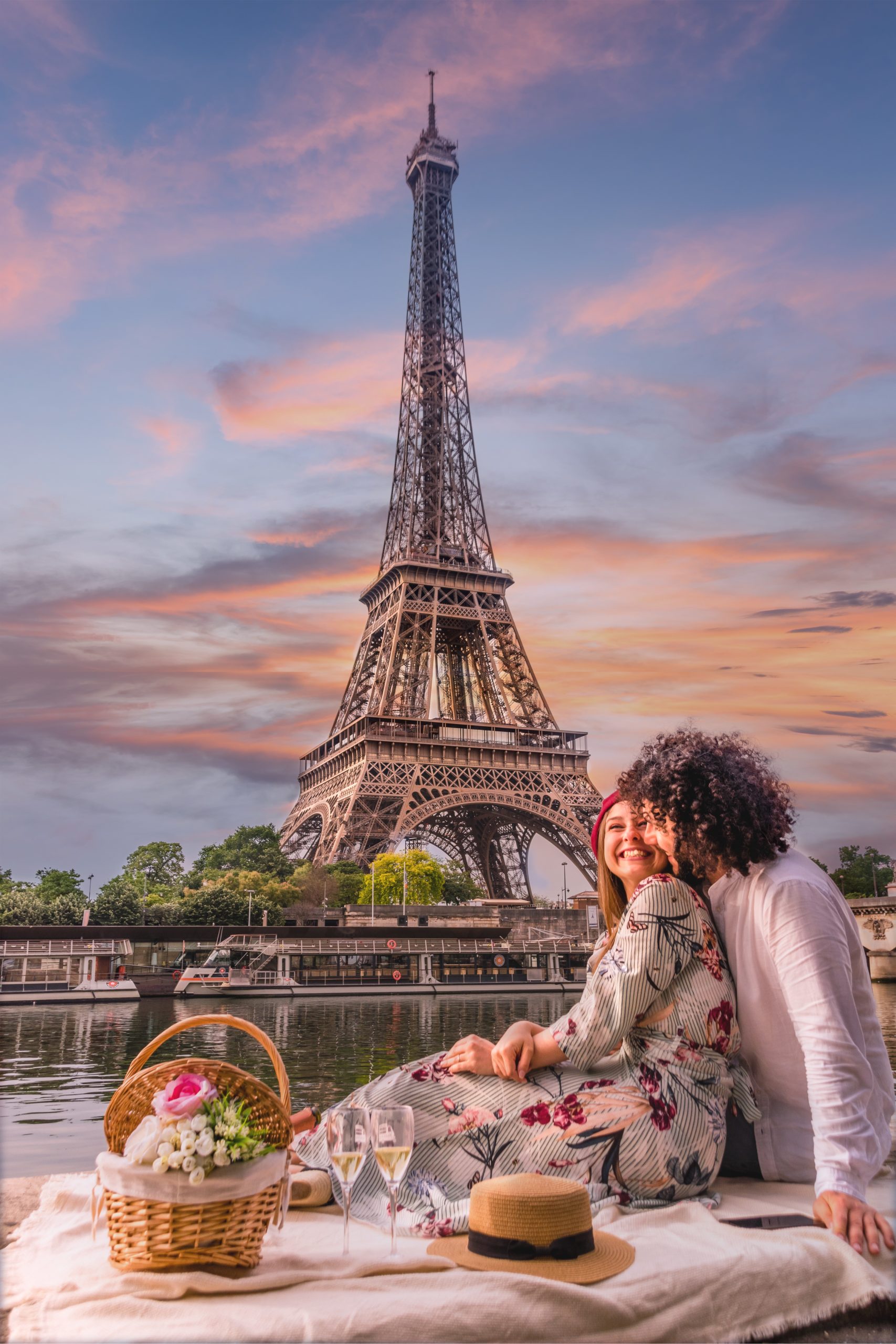 PARIS, FRANCE - Jun 07, 2019: A happy couple is celebrating love with a picnic, wine and flowers with the view of the Eiffel Tower and the Seine river at sunset.